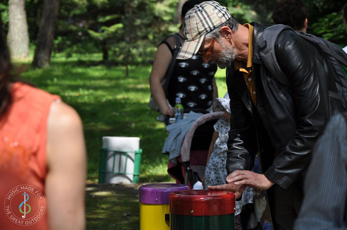 Older man in park playing on a pair of colourful conga drums 