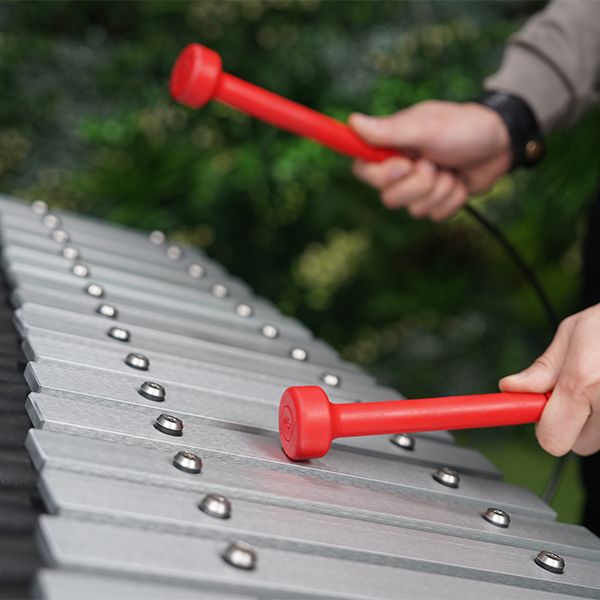 close up image of an outdoor xylophone being played with red mallets