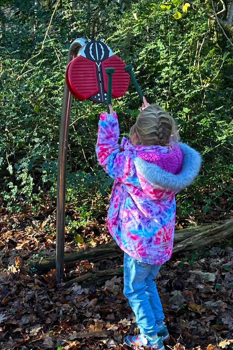 an outdoor musical instrument shaped like a giant red bug on a stainless steel post in the woods