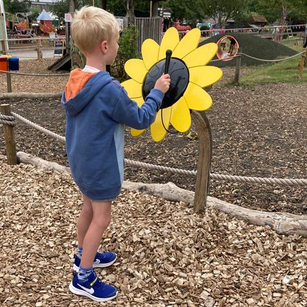 A young boy with blond harir playing a musical drum shaped like a large sunflower in the musical playground at Bockett's Farm