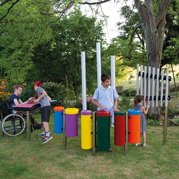 group of four children playing on an ensemble of outdoor musical instruments in a park