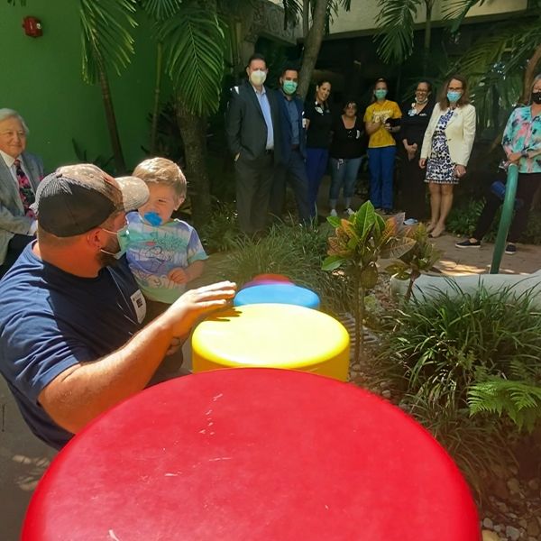 father and son playing five colorful outdoor musical drums in the Palm Beach Children's Hospital  musical dinosaur garden