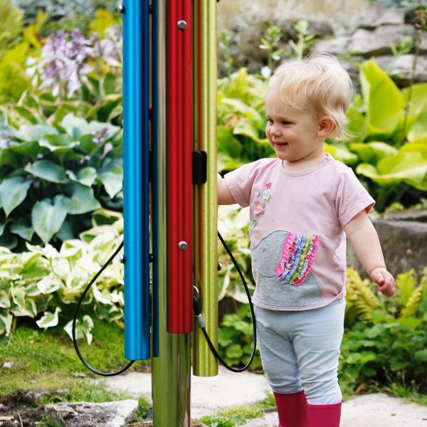 a little girl smiling and playing a musical chime post with four rainbow colored notes and red beater outdoors