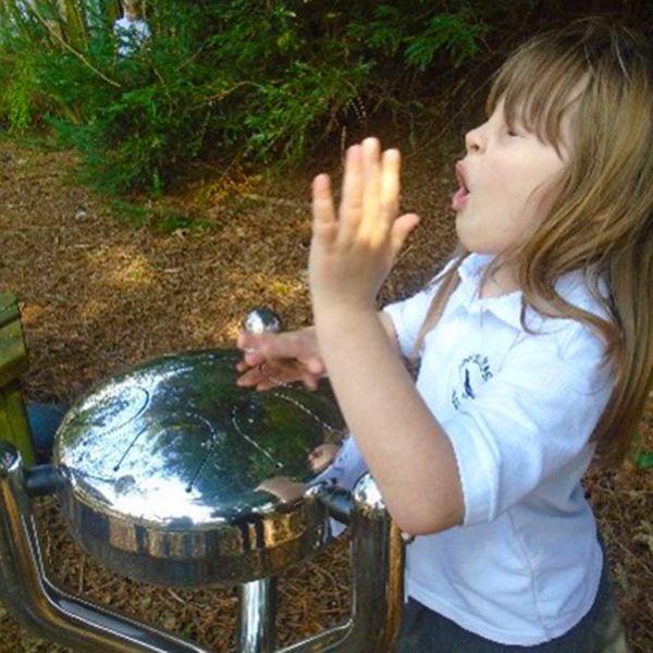 young girl wearing white t shirt playing an outdoor stainless steel tongue drum