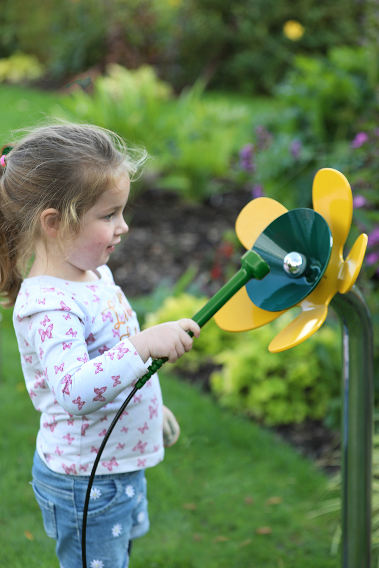 a young girl playing a yellow and green musical flower outdoors in a sensory garden