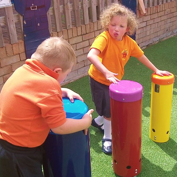 young child standing hitting large outdoor drum with their hands in special needs school playground