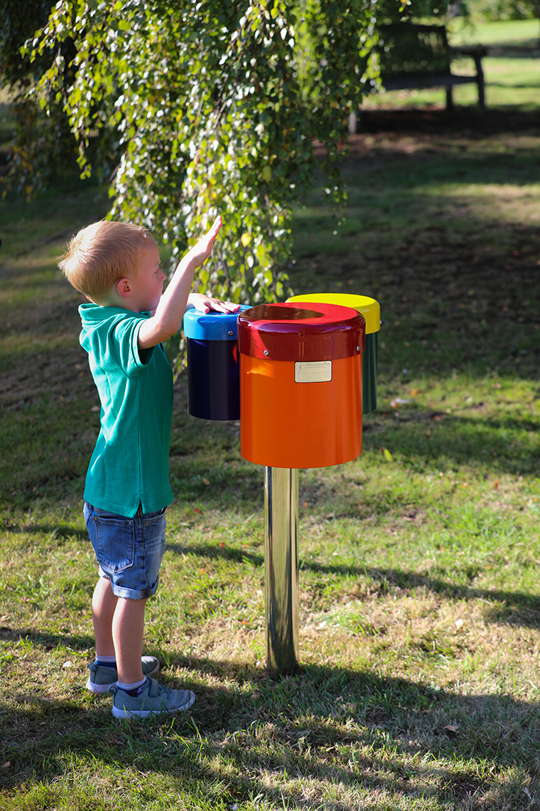 a young boy playing on a set of three colourful outdoor drums in a playground
