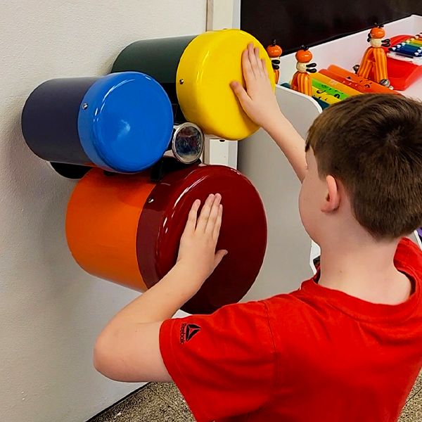 a boy in a red t shirt kneeling and playing a set of three bongo drums attached to the wall