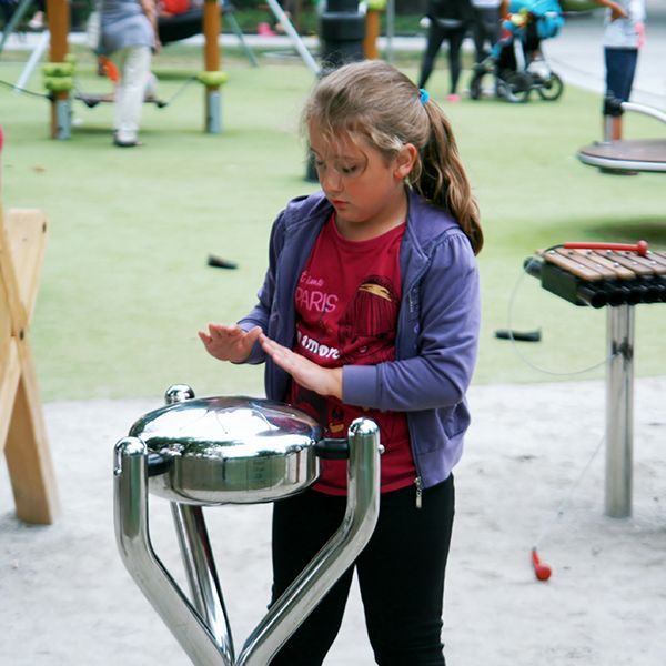 Young girl playing a silver steel tongue drum in a playground