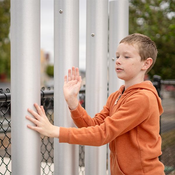 Young boy playing large musical tubular bells in McLaren park