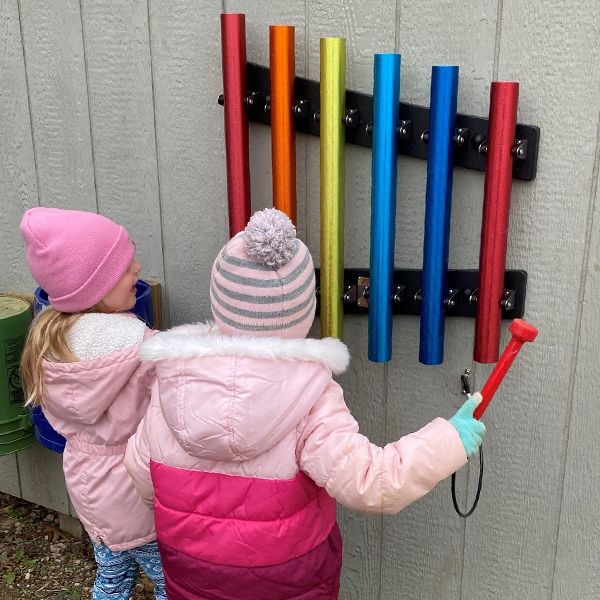 two young girls in winter hats playing rainbow musical chimes hanging on a wall