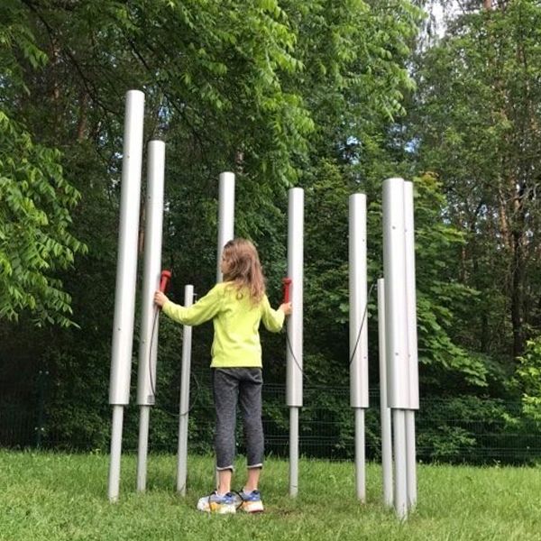 a young girl playing on seven aluminium chimes installed in the ground in a music park