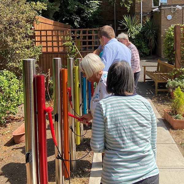 a group of seniors walking along a path with colorful outdoor musical instruments on the side