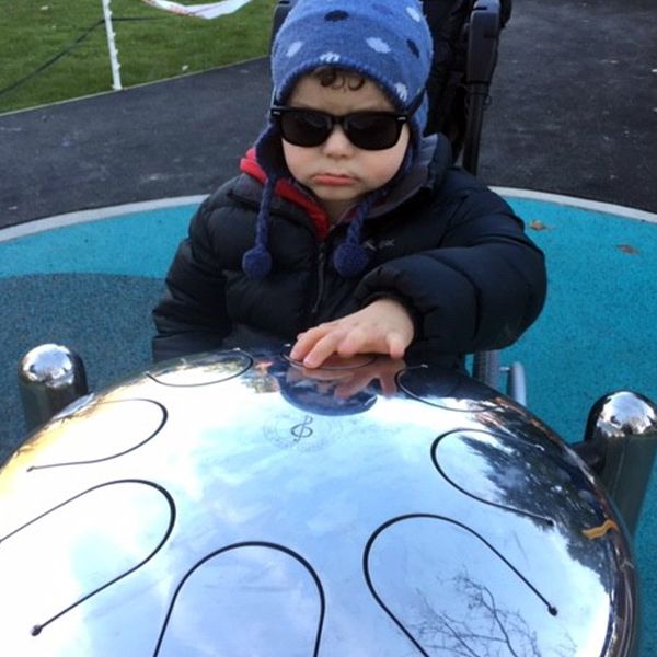 a disabled boy in a wheelchair playing on a silver tongue drum in an inclusive playground