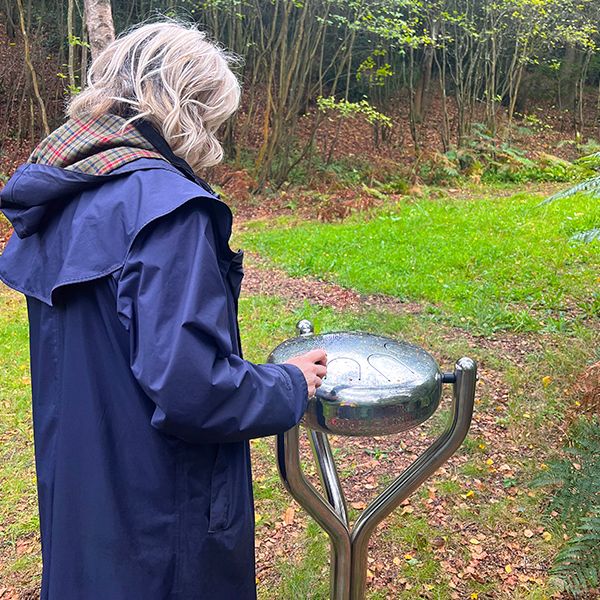 the back of a lady playing a stainless steel outdoor tongue drum called a babel drum