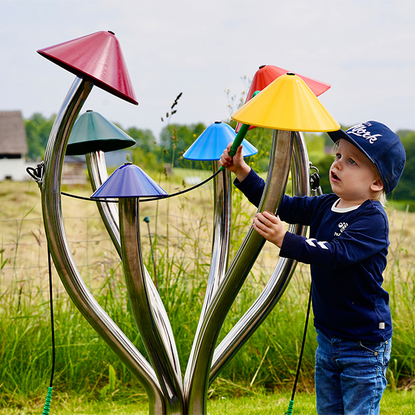 a young boy wearing a cap playing a large outdoor musical instrument shaped like field mushrooms with different coloured caps on each stalk