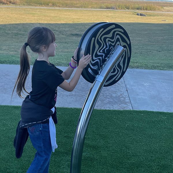 a young girl playing on a large rain wheel in the Kansas Wetlands Center new musical garden