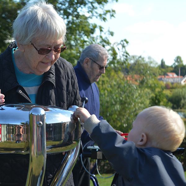 Elderly lady and small boy playing an outdoor stainless steel tongue drum in care home garden