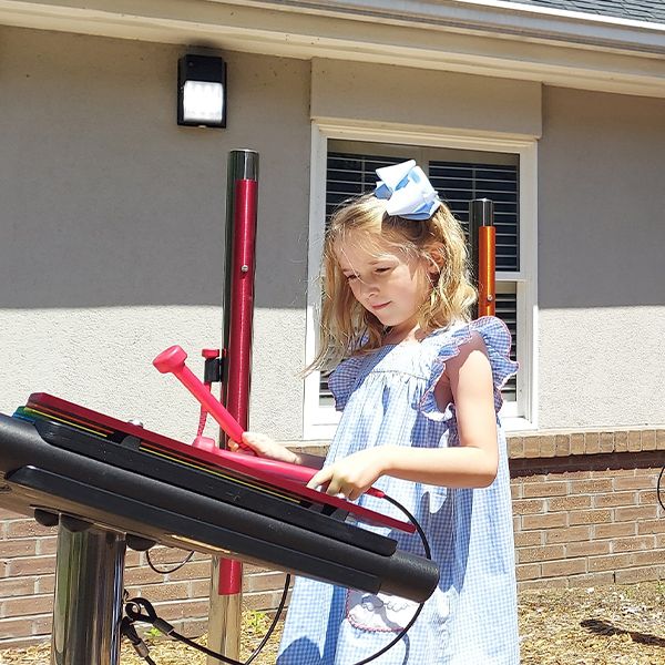 a young white girl playing a rainbow colored outdoor xylophone in a musical church courtyard