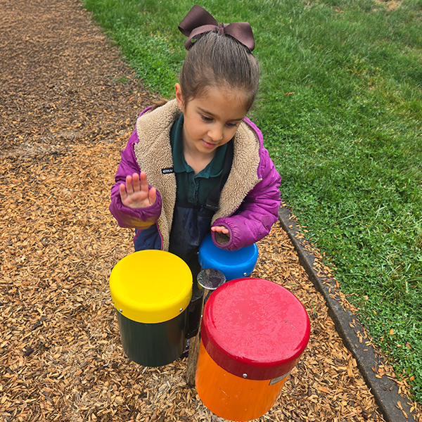 a young girl playing a colorful set of three outdoor bongo drums in a school playground