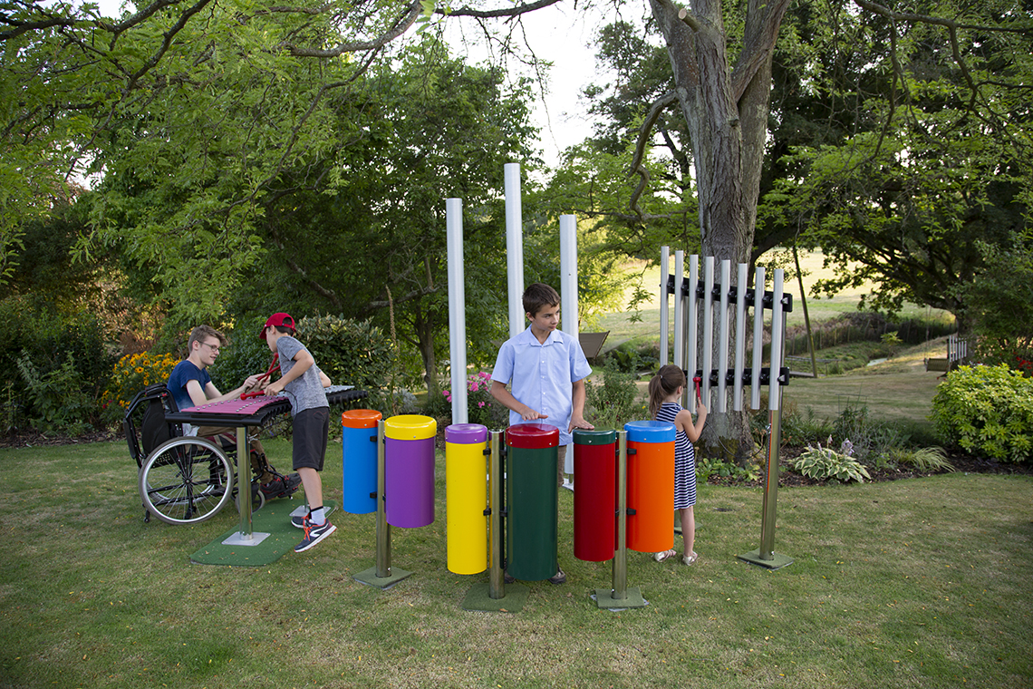 group of four children playing on an ensemble of outdoor musical instruments in a park