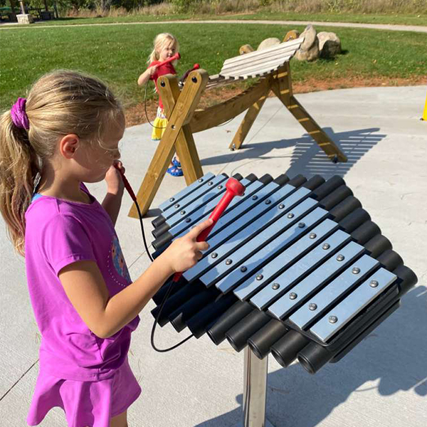a young girl playing on a large outdoor xylophone in a music park