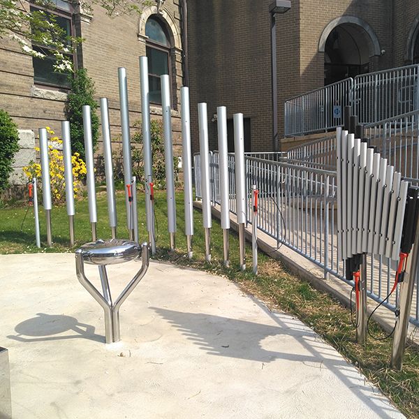 Tall silver-colored musical chimes, a stainless steel tongue drum and upright xylophone installed outside the oil city library