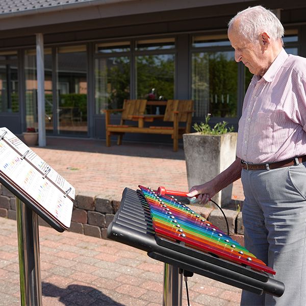 senior male playing a rainbow coloured outdoor xylophone in a care home garden