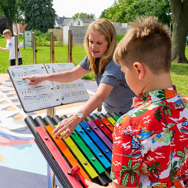 a young boy being taught how to play a large outdoor xylophone in a music park