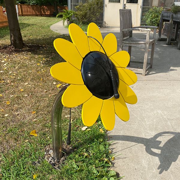 an outdoor yellow and black outdoor drum shaped as a sunflower in a school playground