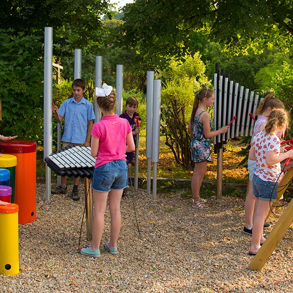 large group of children playing on an ensemble of outdoor musical instruments in a park