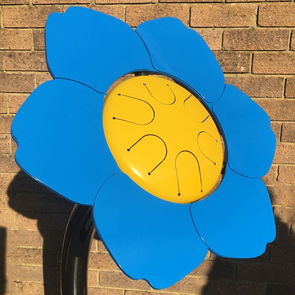 a bright blue and yellow outdoor musical flower drum shaped like a forget me not dementia logo