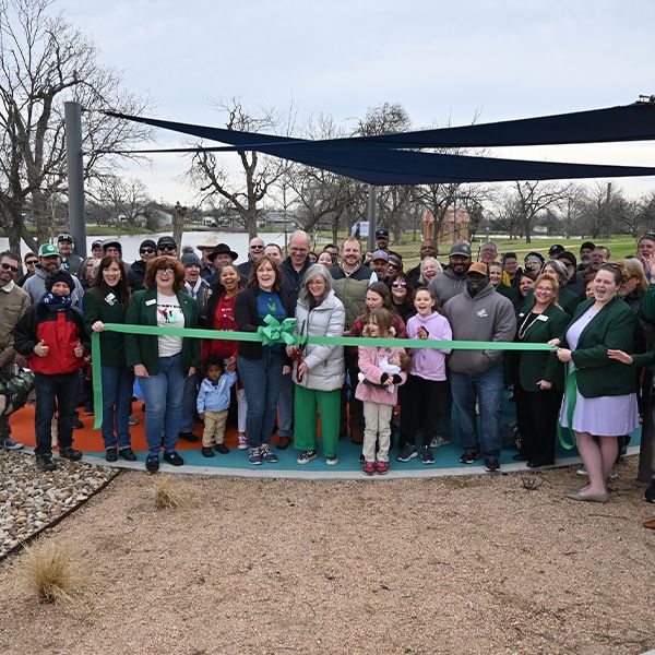 a large group of people standing behind a green ribbon ready to be cut