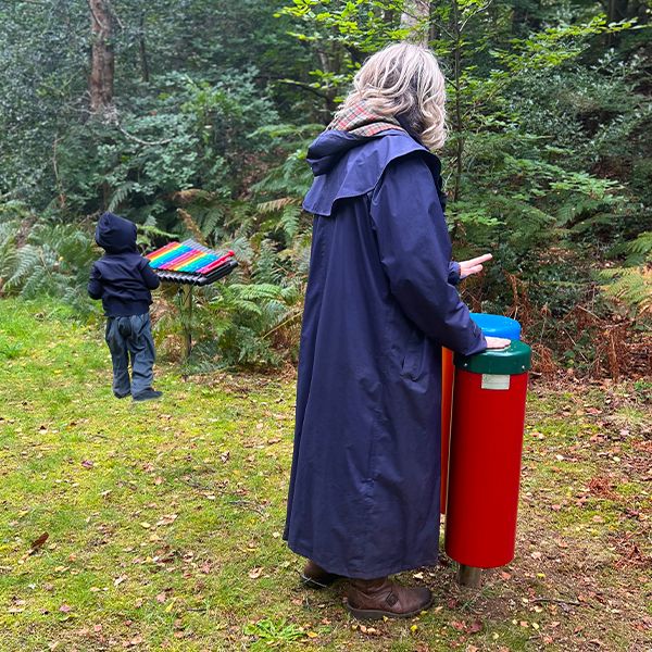 a lady playing a pair of outdoor conga drums with a child in the background playing an outdoor xylophone