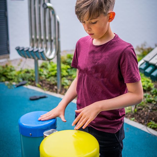 teenage boy plays blue and yellow conga drums in the jess mackie music garden edinburgh children's hospital