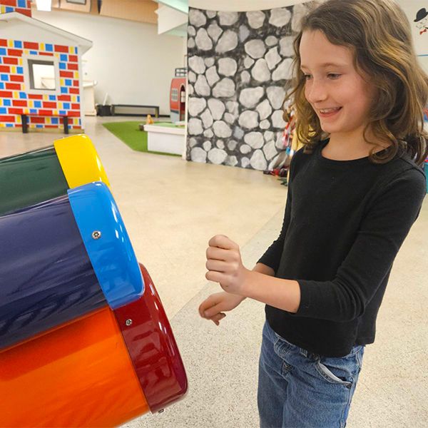 a young girl playing a set of three colourful bongo drums attached to a wall in the baraboo childrens museum