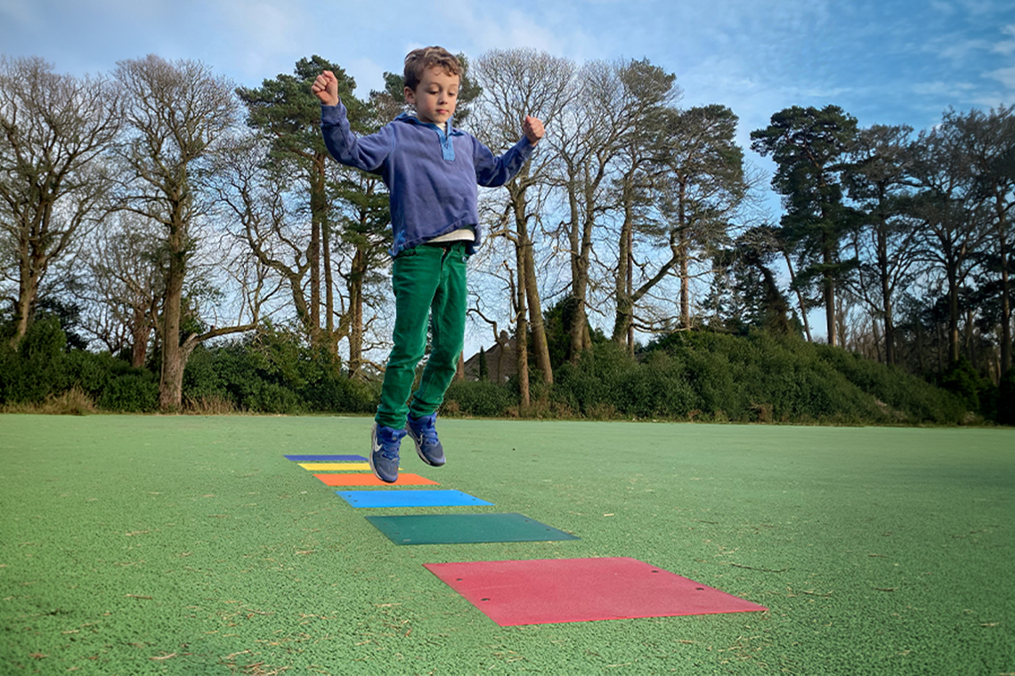 a young boy jumping across colored squares imbedded in the ground that hide musical notes