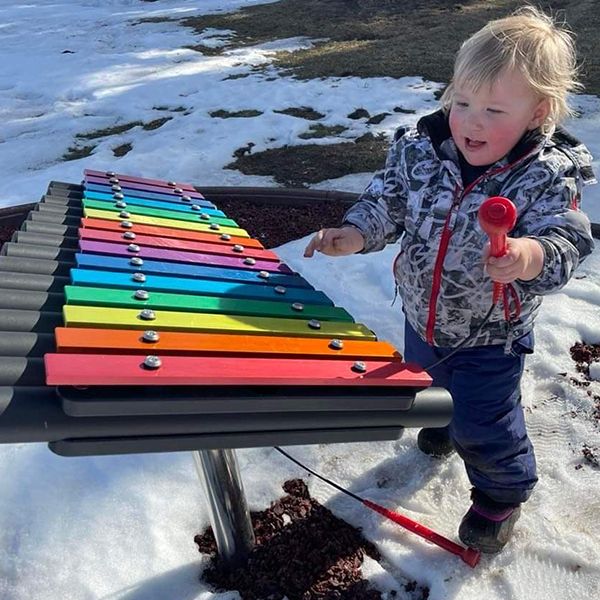 small child in the snow playing a rainbow colored outdoor xylophone