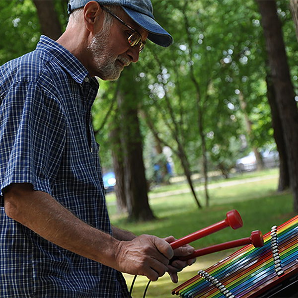 A senior man playing a colourful outdoor xylophone in a musical wellness grove within a park