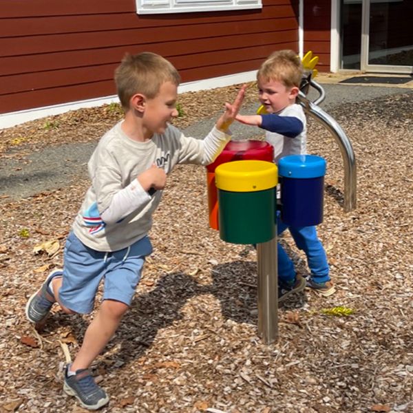 two little boys running around a post with three colourful bongo drums 