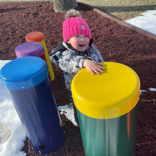 small child in the snow playing a rainbow colored outdoor xylophone