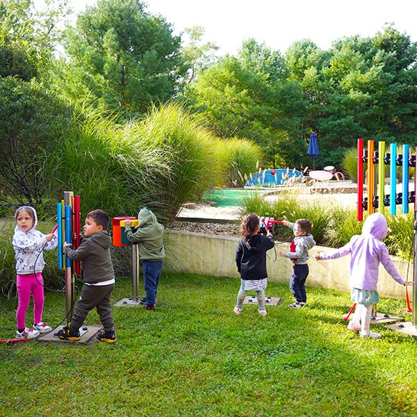 several young children playing on an outdoor ensemble set of rainbow colored small outdoor musical instruments in a museum sensory garden