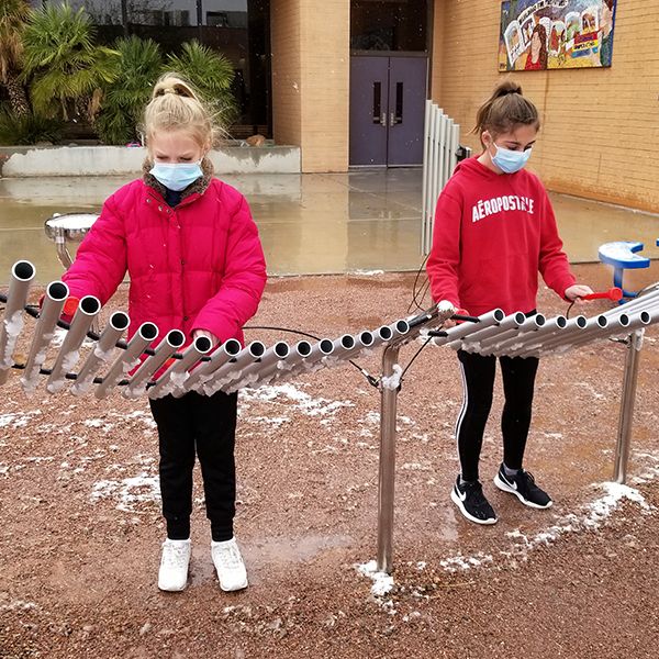 two schoolgirls wearing a red uniforms playing an outdoor musical instrument in the school playground