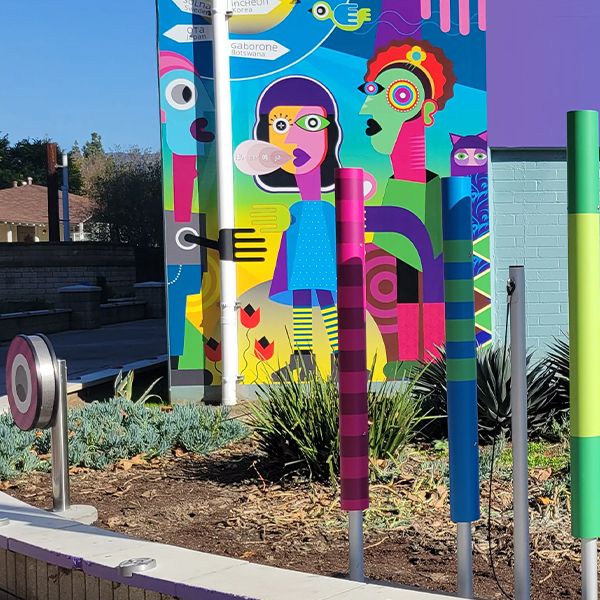 outdoor musical chimes installed in the ground and wrapped in varied colorful vinyl alongside a bright colorful rainwheel