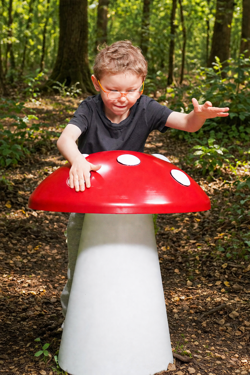 Young boy in a woodland playing a large outdoor musical toadstool by pressing the white spots on its red cap