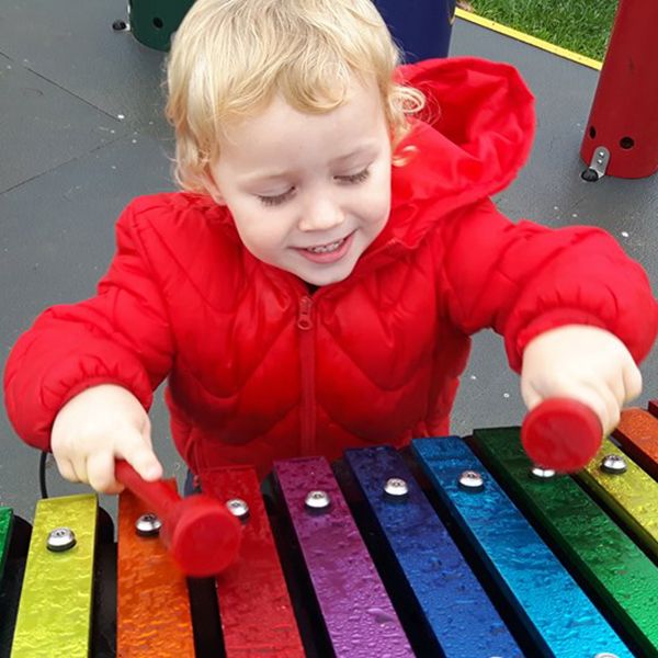 young boy playing on an rainbow coloured outdoor xylophone in a Farm Park playgound