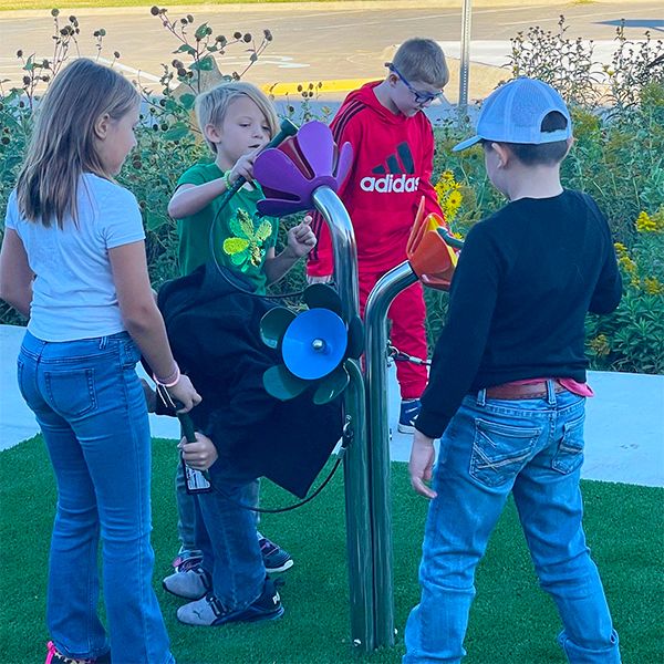 a group of scholl age children playing on an outdoor musical instrument shaped like flowers in the Kansas Wetlands Center new music garden