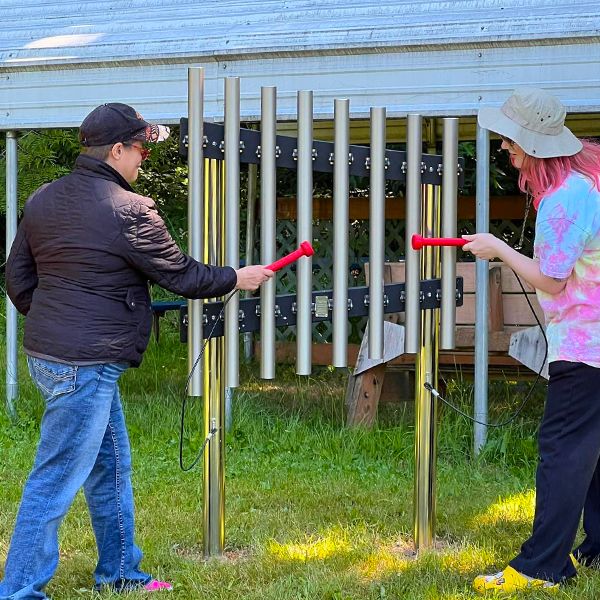 A man and a woman playing a set of silver outdoor musical chimes in the camp beausite new musical garden