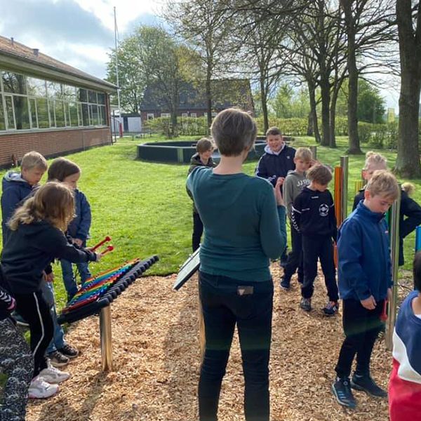 a class of danish schoolchildren playing on new outdoor musical chimes and xylophone in their new outdoor music garden