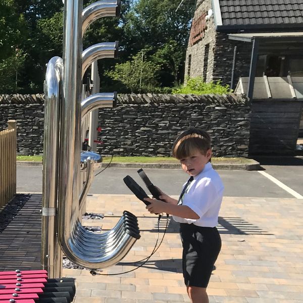 a young boy in school uniform playing a large outdoor musical instrument with curled pipes called tembos